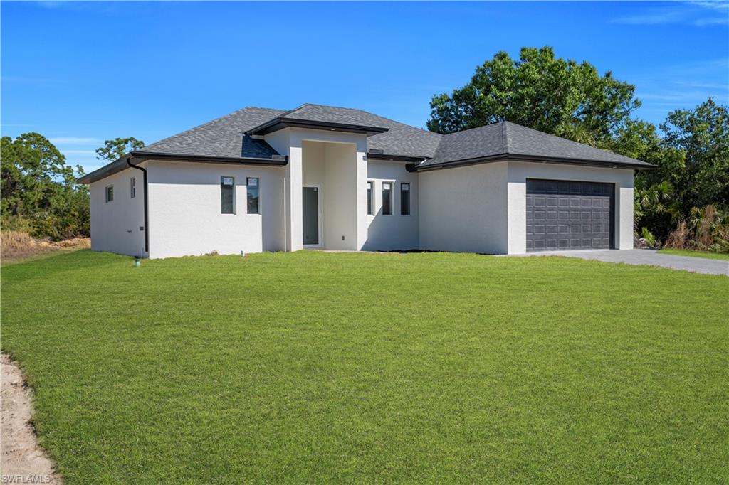 Prairie-style house featuring a front lawn, an attached garage, stucco siding, and driveway
