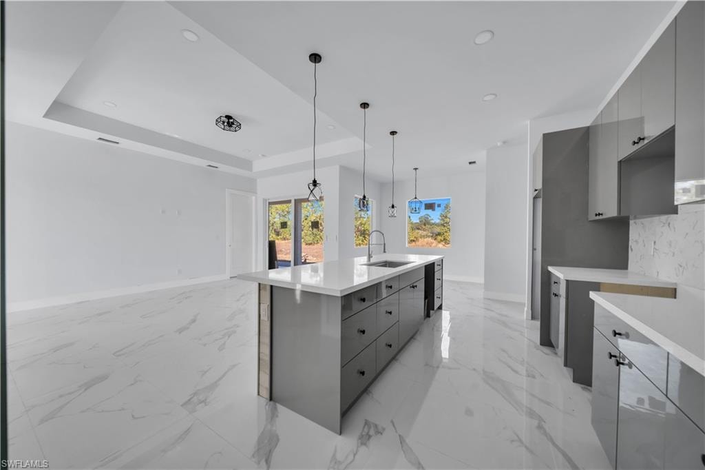 Kitchen with modern cabinets, an island with sink, light stone countertops, gray cabinets, and pendant lighting