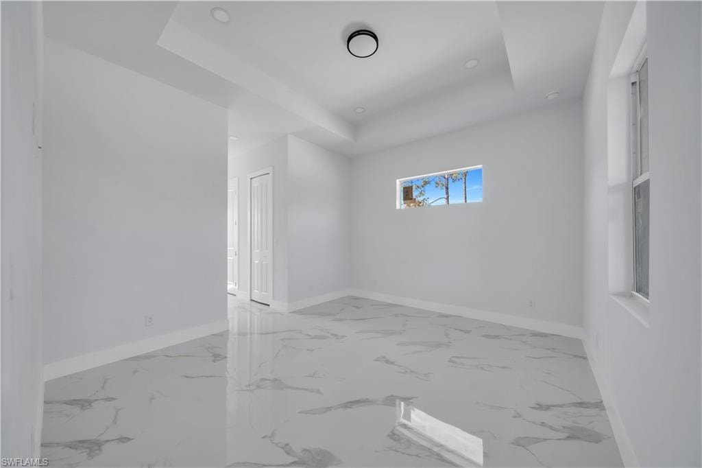 Unfurnished room featuring a tray ceiling and light marble finish flooring
