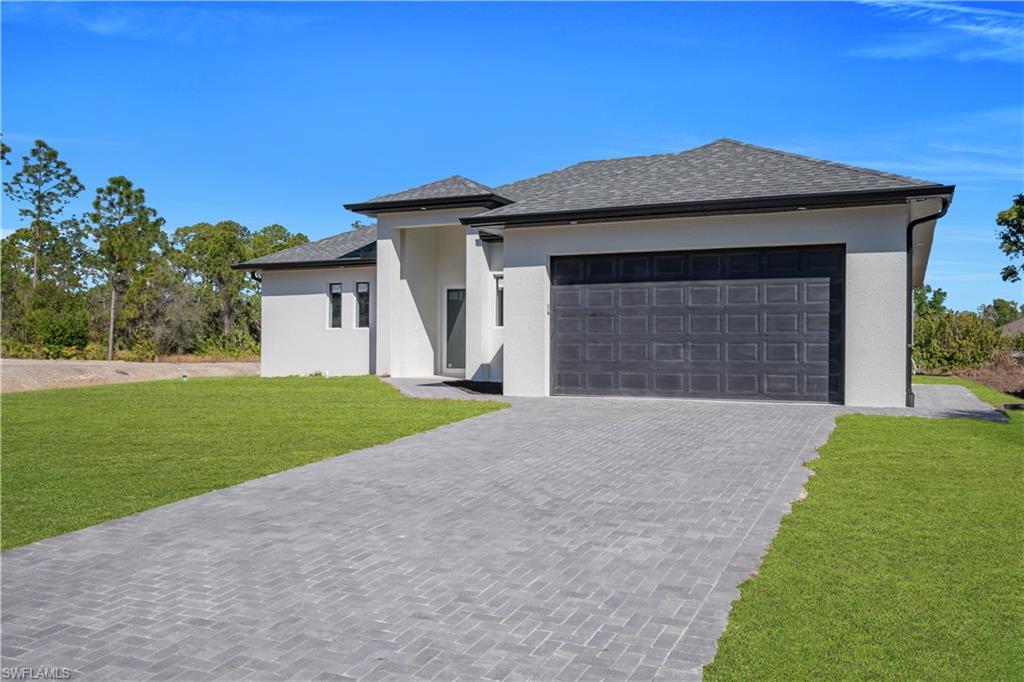 Prairie-style house featuring a front yard, driveway, an attached garage, stucco siding, and a shingled roof
