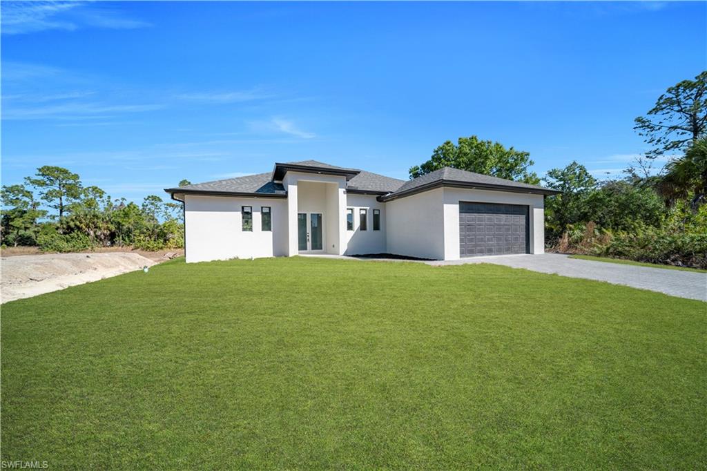Prairie-style house featuring a front yard, driveway, stucco siding, and an attached garage