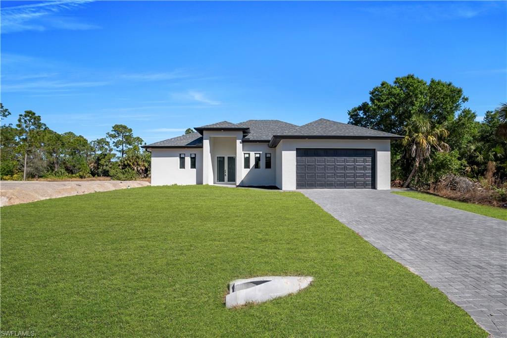 Prairie-style home featuring a front yard, decorative driveway, stucco siding, and a garage