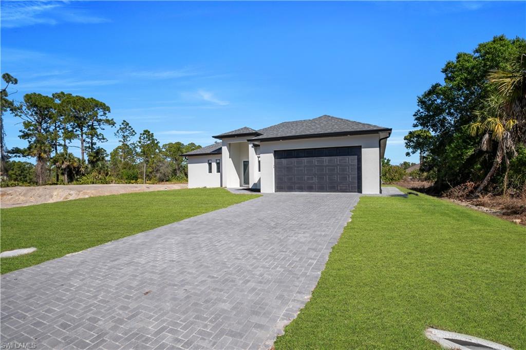 Prairie-style home featuring a front yard, driveway, stucco siding, a garage, and a shingled roof