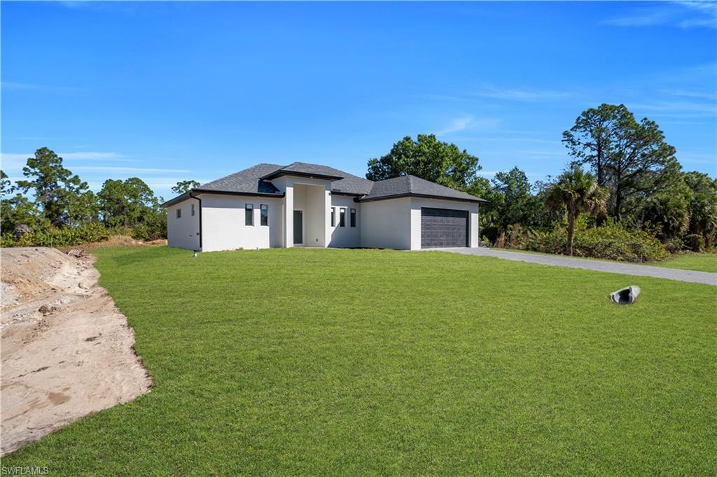 Prairie-style home featuring driveway, a front yard, an attached garage, and stucco siding