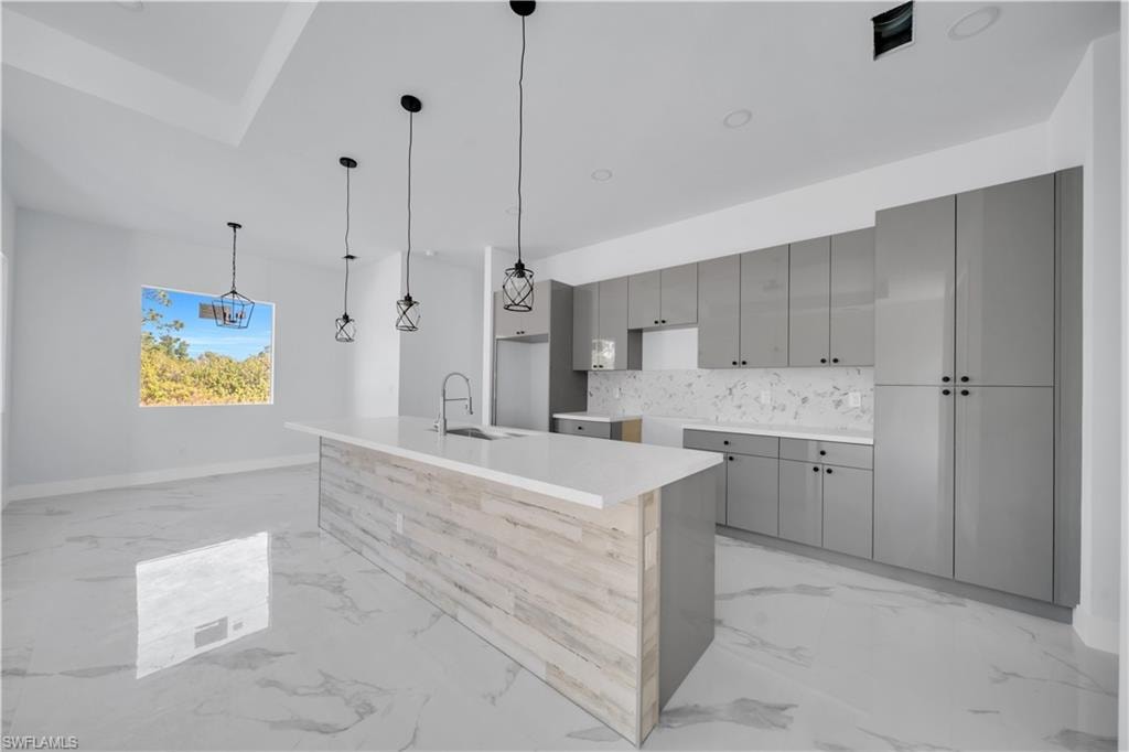 Kitchen with gray cabinetry, a center island with sink, modern cabinets, pendant lighting, and decorative backsplash