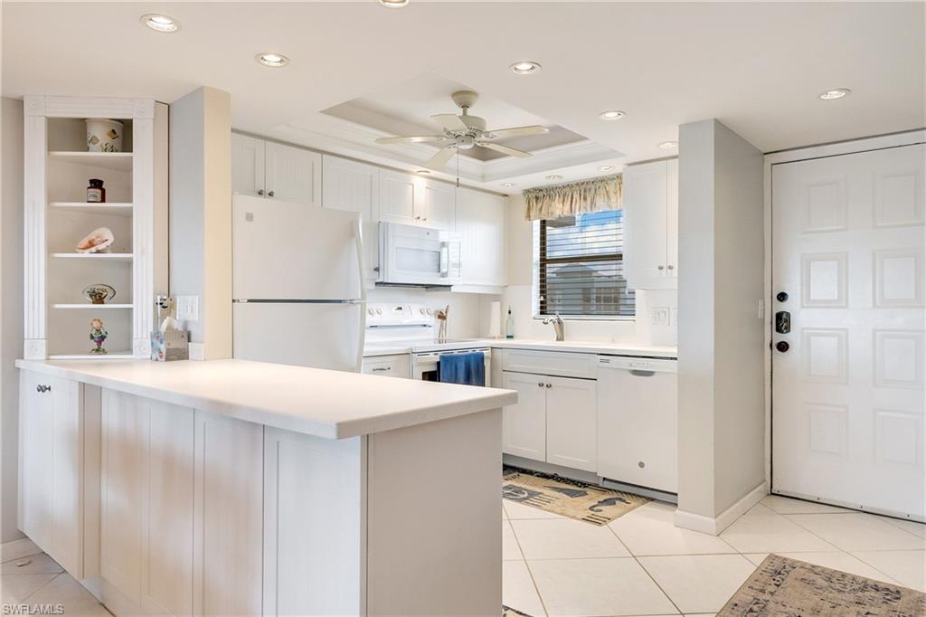 Kitchen with white appliances, a raised ceiling, white cabinets, light countertops, and a peninsula
