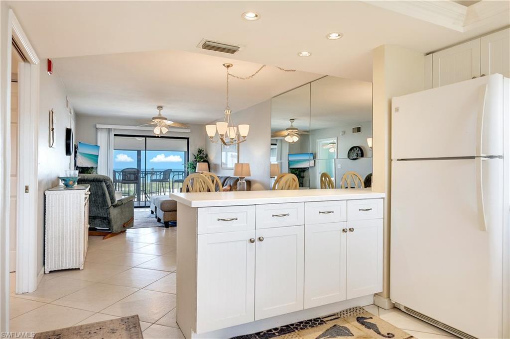 Kitchen with open floor plan, freestanding refrigerator, white cabinets, suspended lighting, and ceiling fan