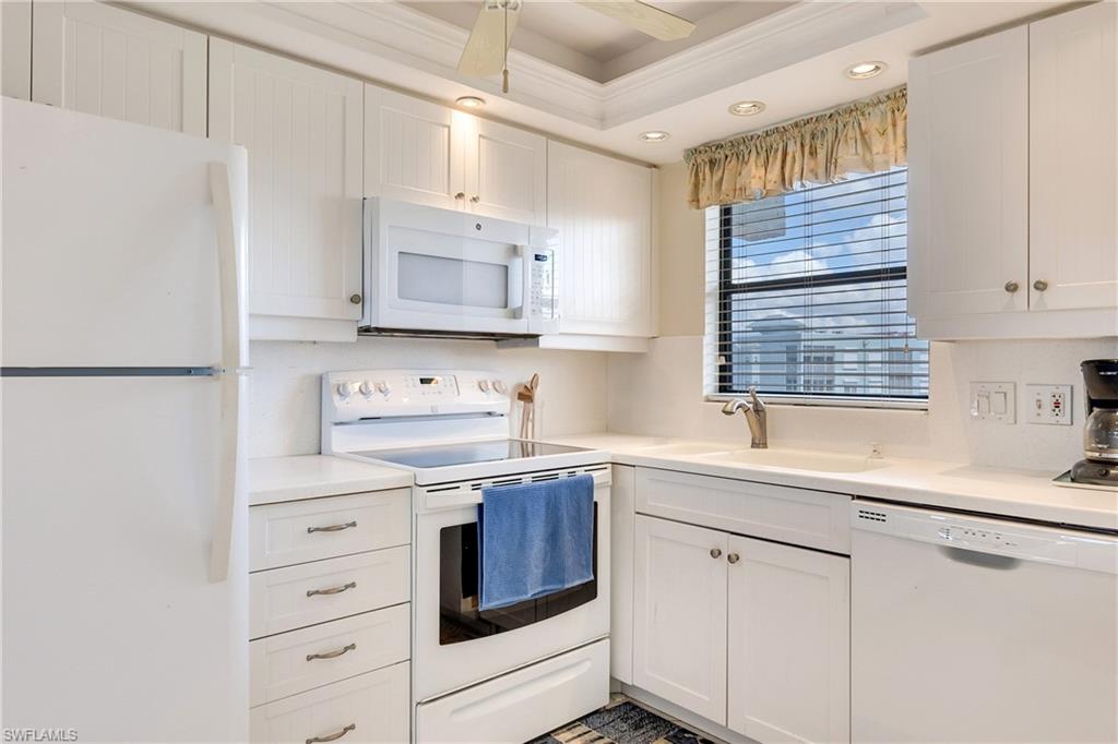 Kitchen with white appliances, white cabinets, light countertops, crown molding, and a ceiling fan