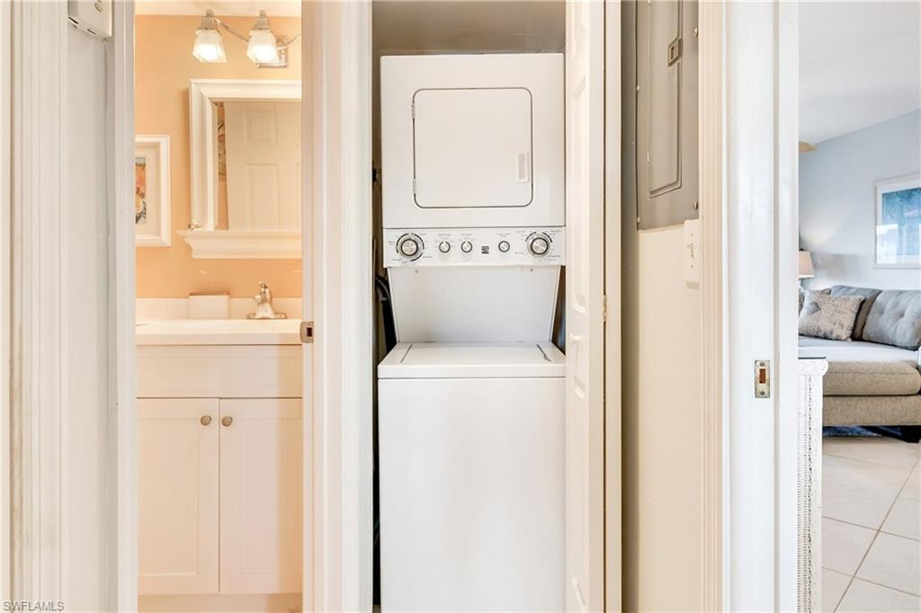 Laundry area with stacked washer / dryer, light tile patterned floors, and electric panel
