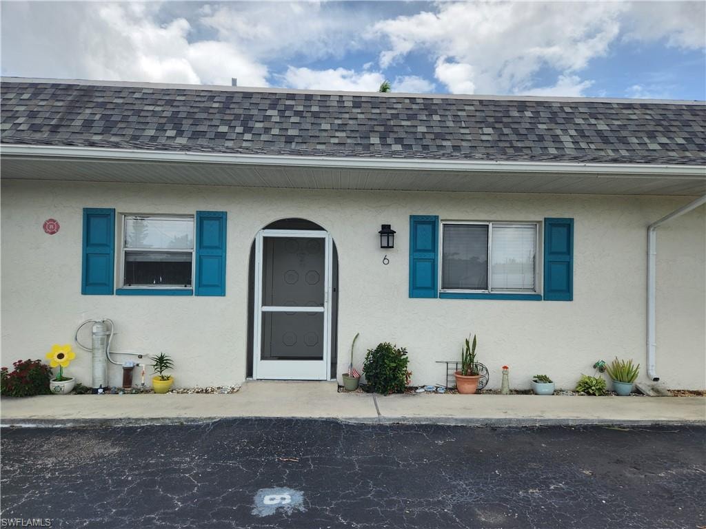 Doorway to property featuring stucco siding and roof with shingles
