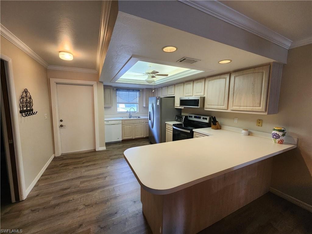 Kitchen featuring crown molding, dark wood finished floors, light countertops, stainless steel appliances, and a peninsula