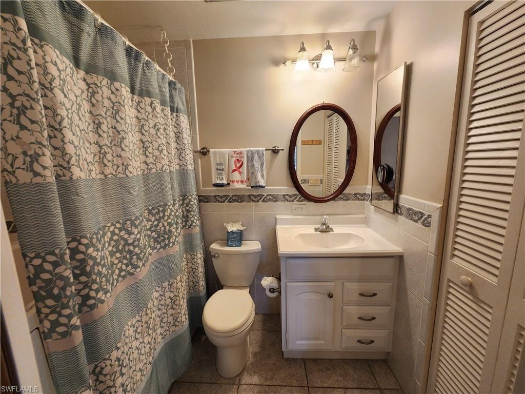 Full bath with a closet, vanity, tile walls, a shower with curtain, and tile patterned flooring
