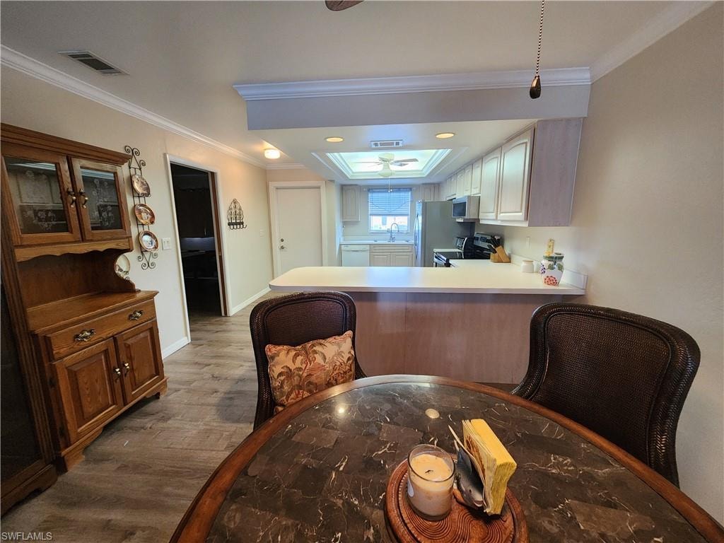 Kitchen featuring dark wood-style flooring, light countertops, a peninsula, stainless steel range with electric stovetop, and ornamental molding
