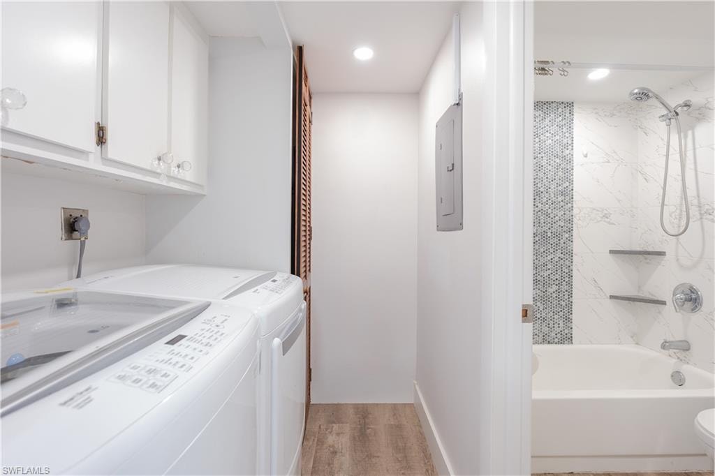 Laundry area featuring light wood-type flooring, electric panel, independent washer and dryer, recessed lighting, and cabinet space