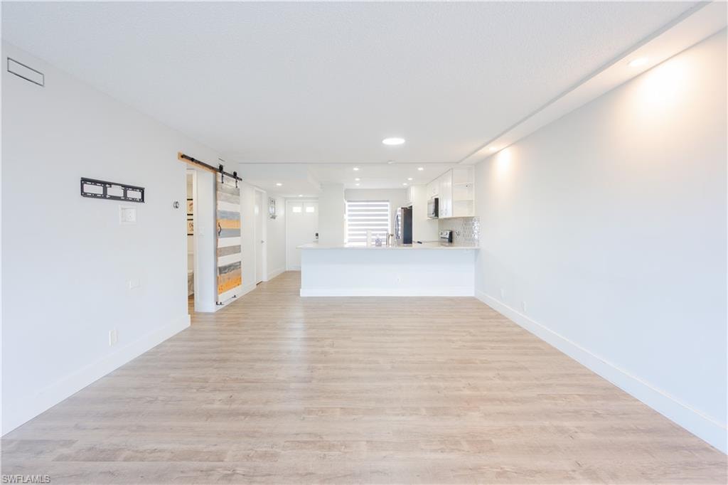 Unfurnished living room with a barn door, light wood-type flooring, and recessed lighting