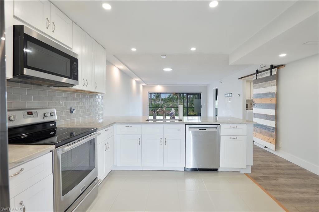Kitchen with stainless steel appliances, a peninsula, white cabinets, a barn door, and recessed lighting