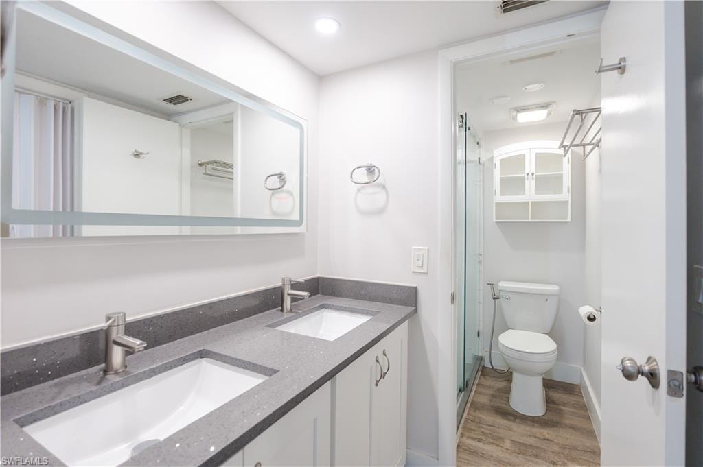 Full bath with double vanity, a stall shower, light wood-type flooring, and recessed lighting