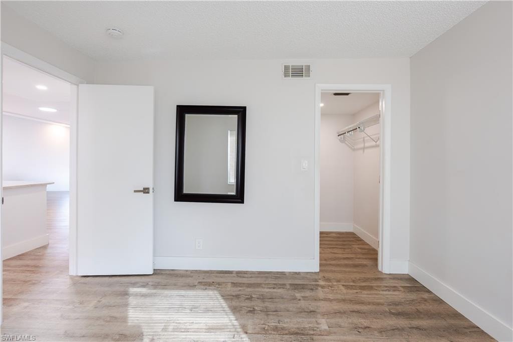 Unfurnished bedroom featuring a spacious closet, light wood-type flooring, recessed lighting, and a textured ceiling