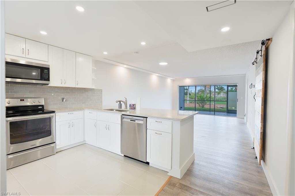 Kitchen with stainless steel appliances, a peninsula, open shelves, white cabinets, and decorative backsplash