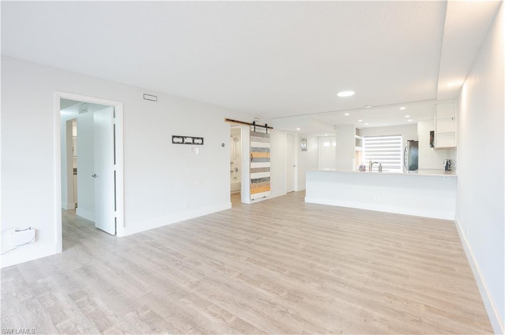 Unfurnished living room featuring a barn door, light wood-type flooring, and recessed lighting