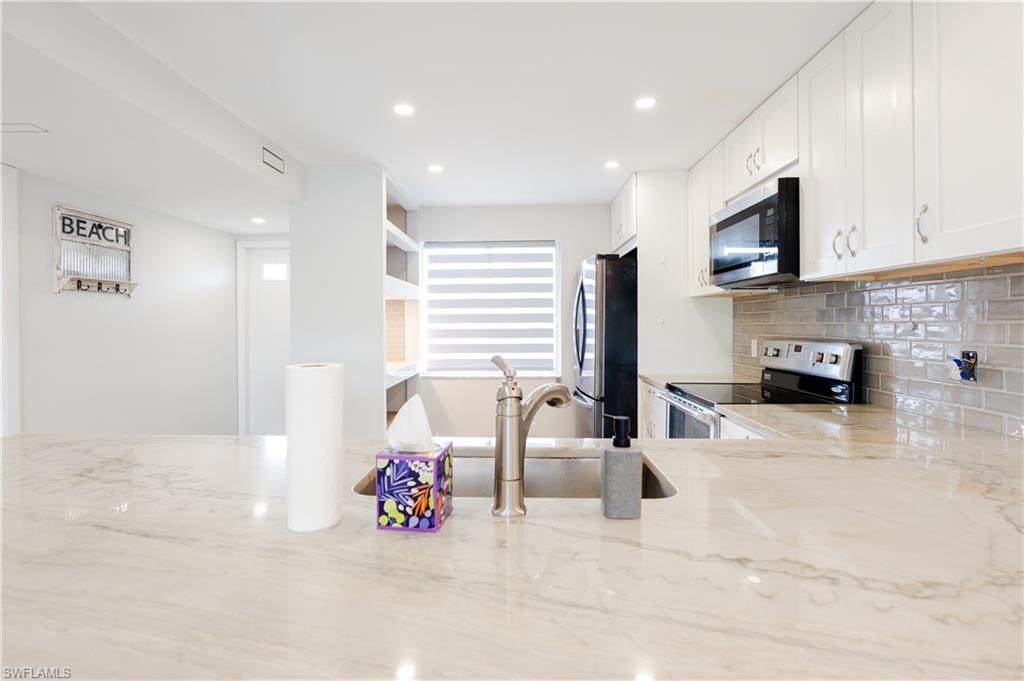 Kitchen featuring stainless steel appliances, light stone countertops, white cabinets, tasteful backsplash, and recessed lighting