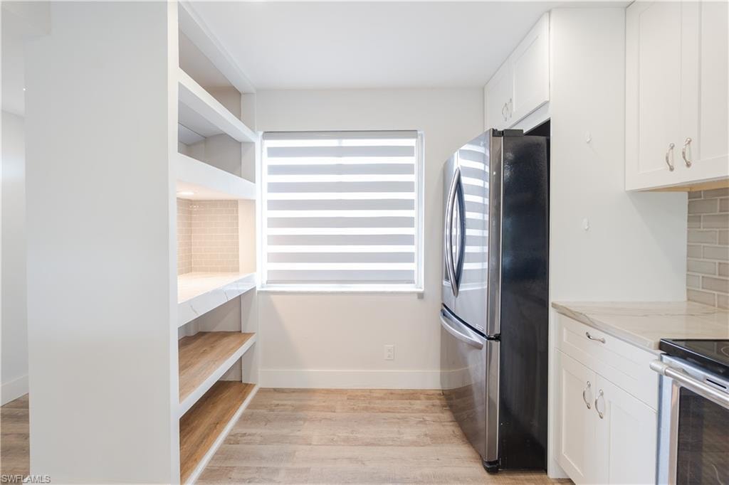 Kitchen featuring white cabinetry, stainless steel appliances, light wood-style flooring, light stone counters, and tasteful backsplash
