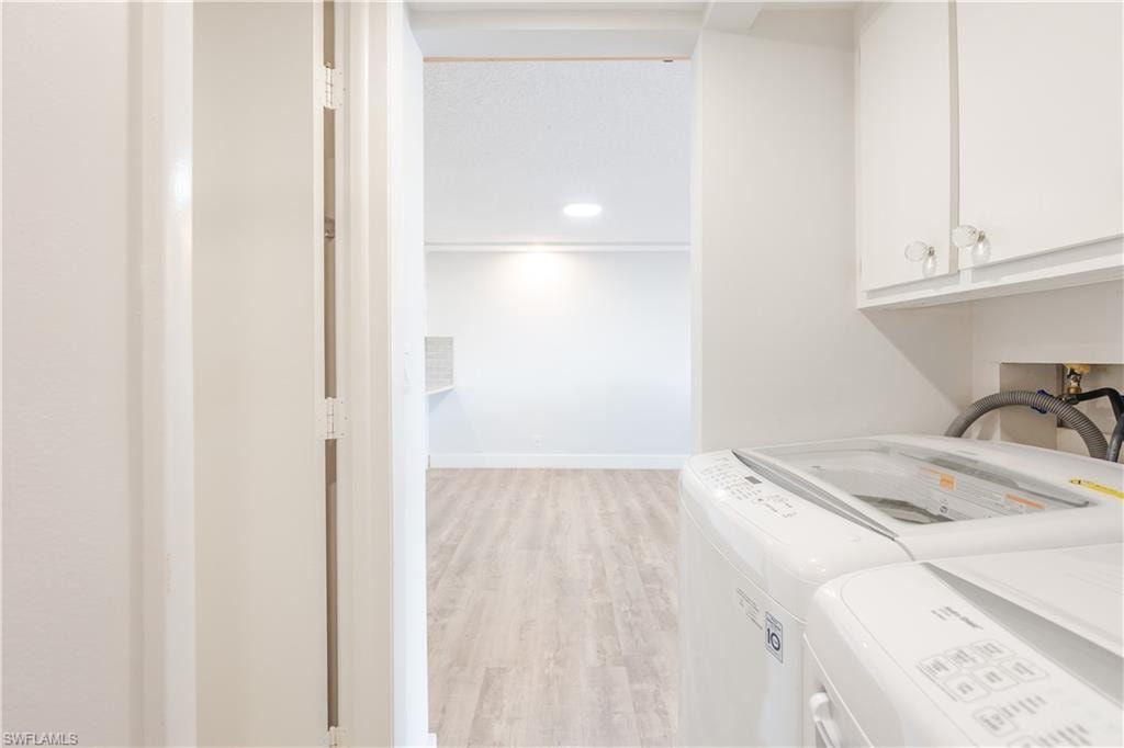 Laundry room with light wood-type flooring, washing machine and clothes dryer, and cabinet space