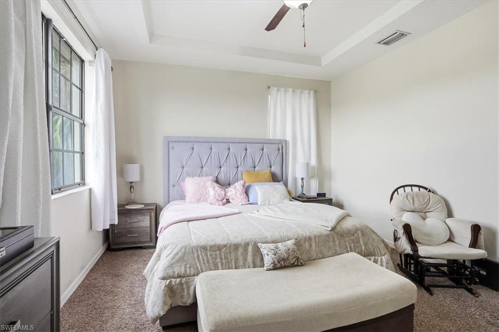 Carpeted bedroom with a raised ceiling and a ceiling fan