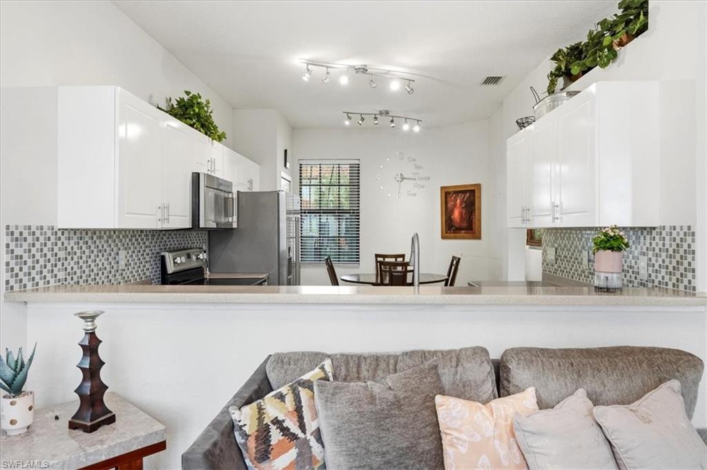 Kitchen featuring decorative backsplash, a peninsula, stainless steel appliances, and white cabinets