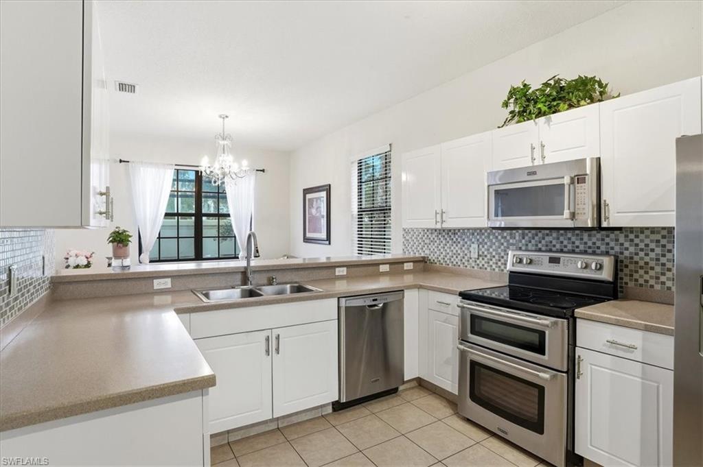 Kitchen with stainless steel appliances, white cabinets, decorative backsplash, hanging lights, and light tile patterned floors