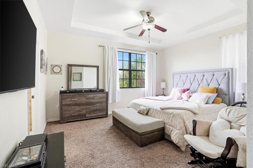 Bedroom featuring dark colored carpet, a ceiling fan, and a raised ceiling