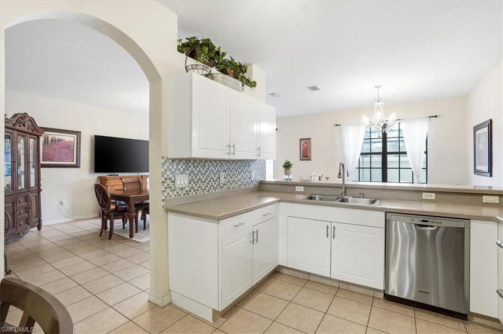 Kitchen featuring stainless steel dishwasher, white cabinets, light countertops, tasteful backsplash, and arched walkways