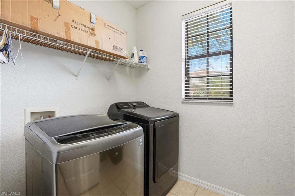 Laundry room featuring a textured wall, washing machine and dryer, and light tile patterned flooring