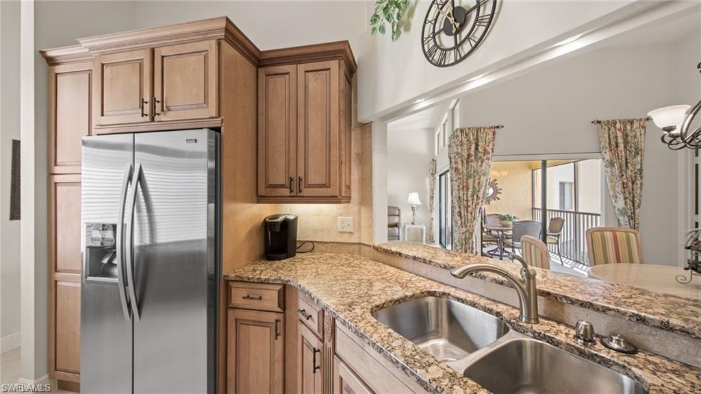 Kitchen featuring stainless steel fridge with ice dispenser, light stone counters, and wood finish cabinetry