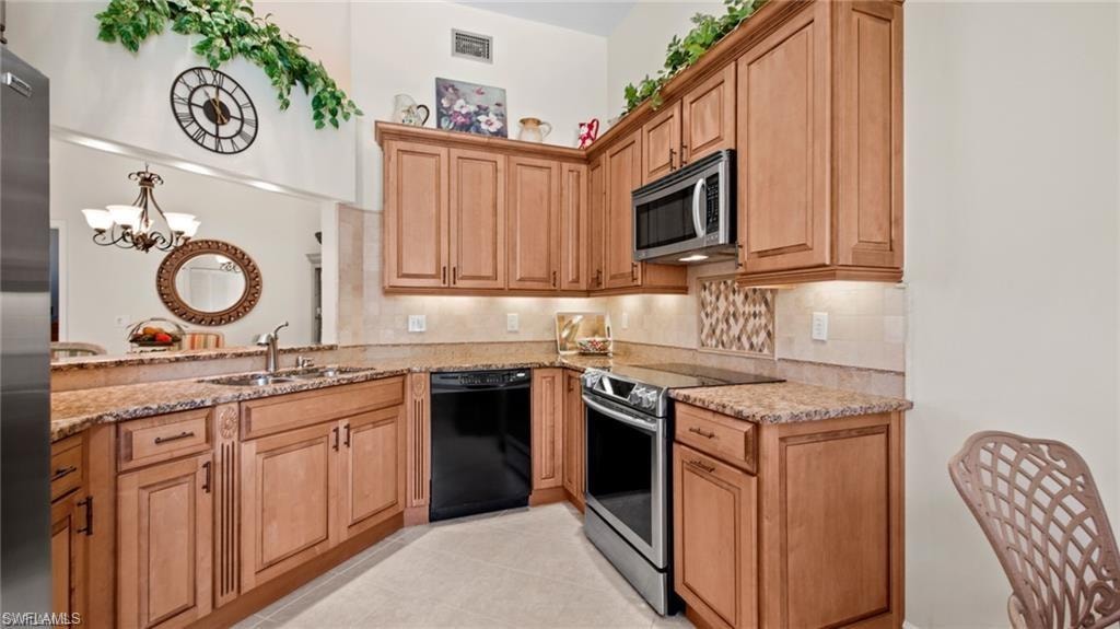 Kitchen featuring stainless steel appliances, light stone counters, backsplash, a chandelier, and light tile patterned floors