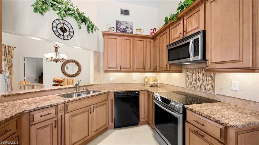 Kitchen with stainless steel appliances, light stone countertops, wood finish cabinetry, and a chandelier