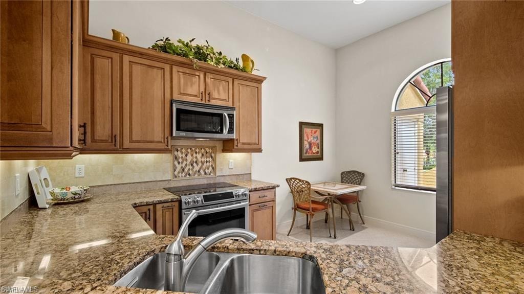 Kitchen featuring light stone countertops, stainless steel appliances, wood finish cabinetry, and tasteful backsplash