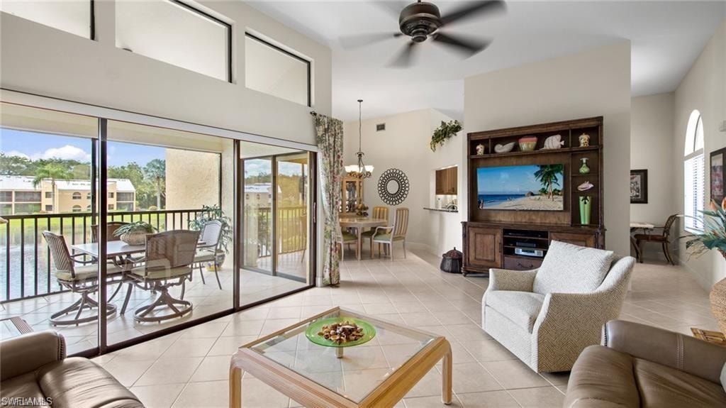 Living room featuring ceiling fan, hanging lights, light tile patterned floors, and a high ceiling