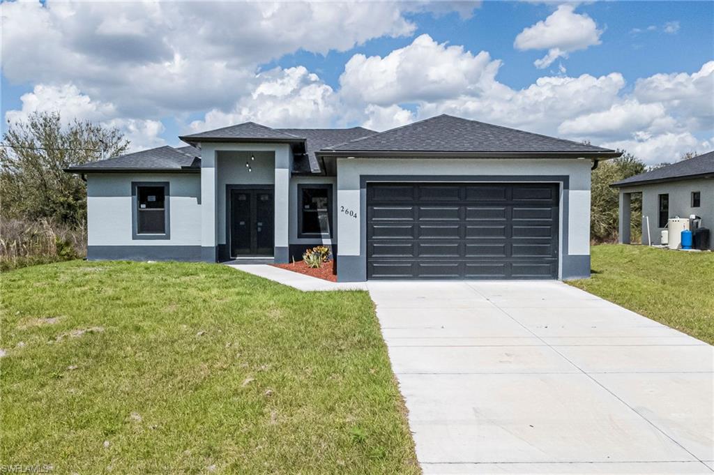 Prairie-style house featuring a front yard, concrete driveway, an attached garage, stucco siding, and a shingled roof