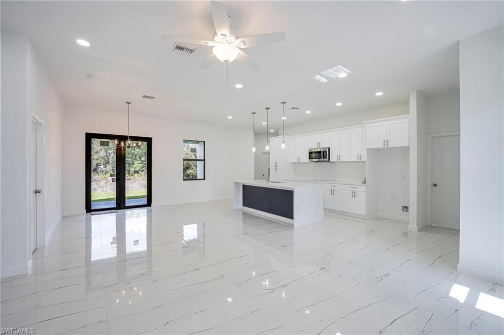 Kitchen with open floor plan, a ceiling fan, white cabinets, a kitchen island with sink, and a chandelier
