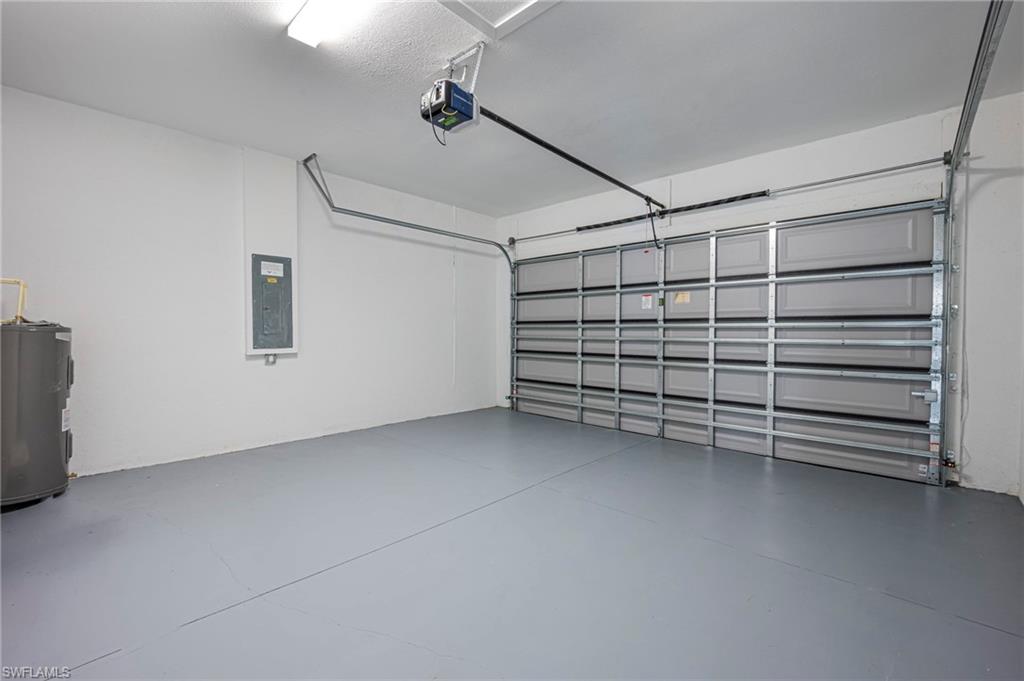 Garage featuring electric water heater, electric panel, and a garage door opener