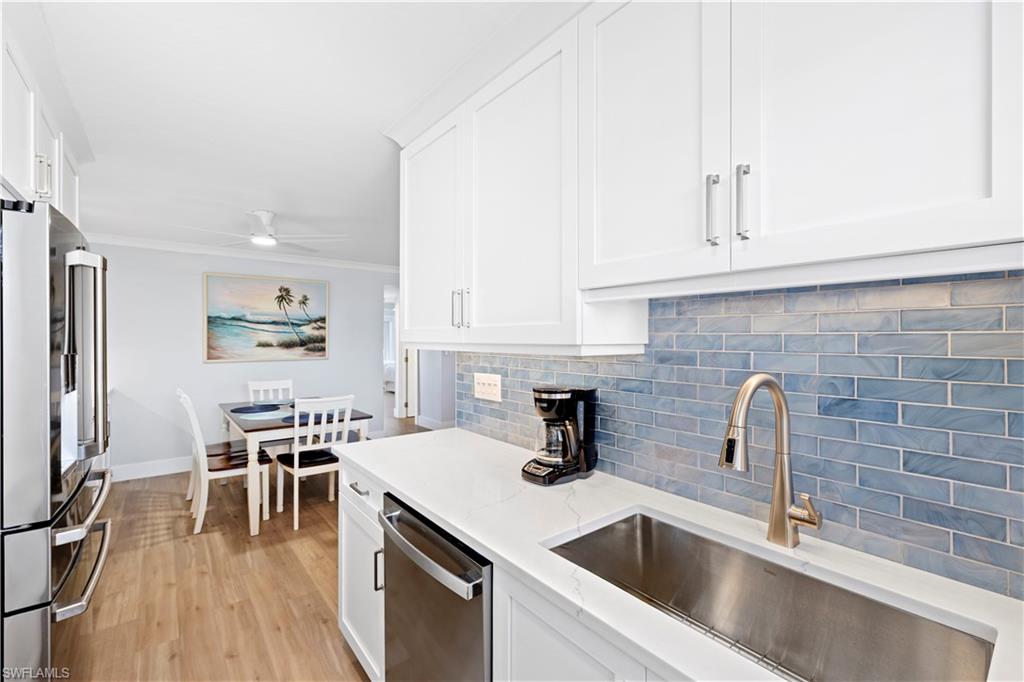 Kitchen with appliances with stainless steel finishes, tasteful backsplash, white cabinets, light wood-type flooring, and a ceiling fan