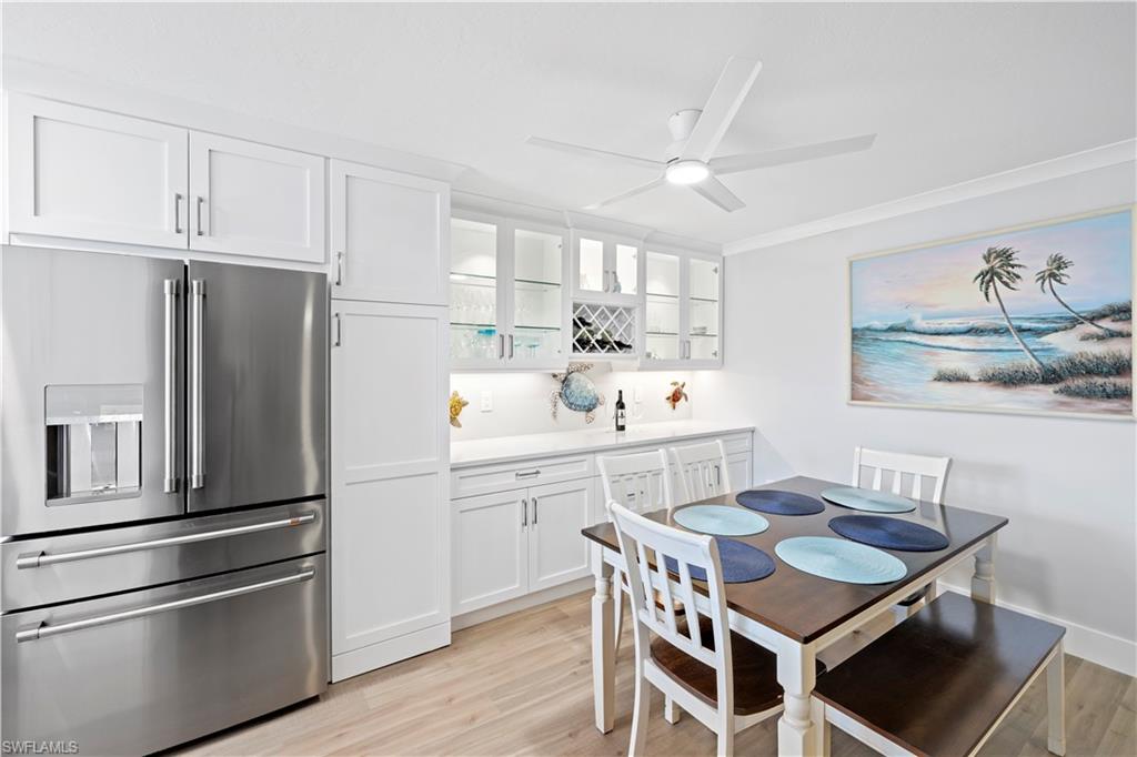 Dining space featuring bar with sink, light wood-style flooring, a ceiling fan, and crown molding