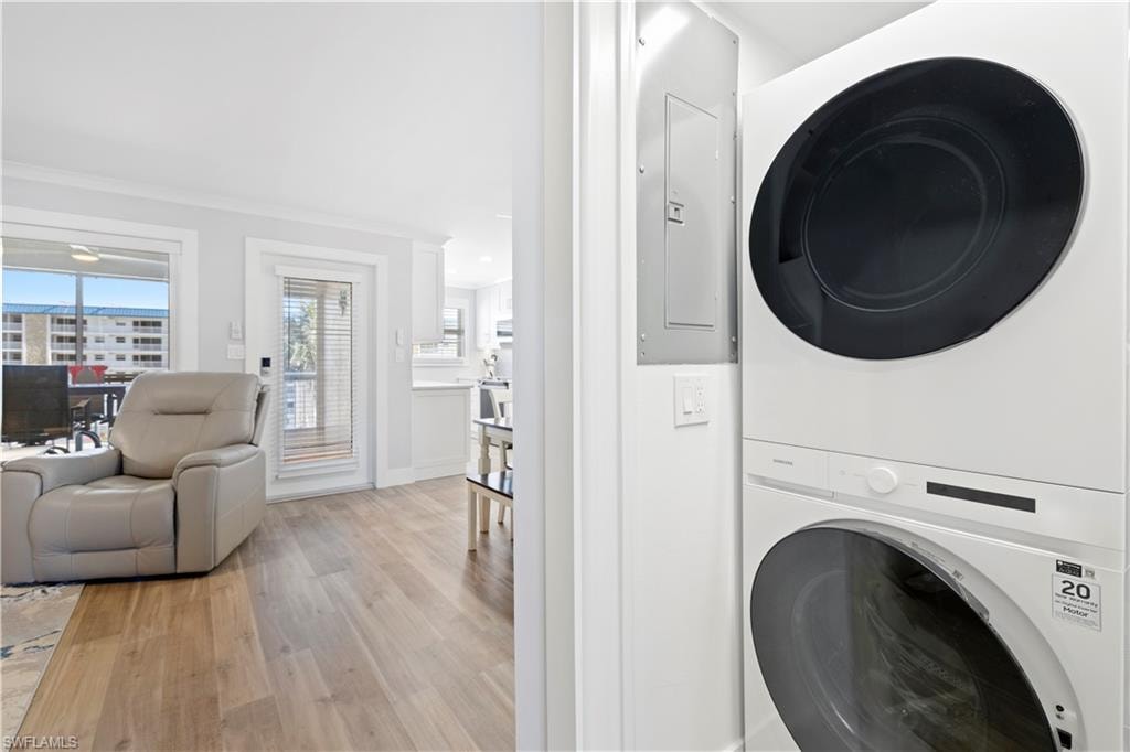 Washroom with stacked washer and clothes dryer, light wood finished floors, crown molding, and electric panel
