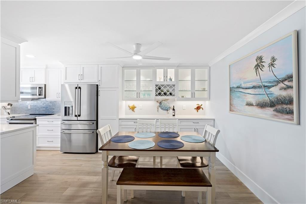 Dining area with light wood-style floors, ceiling fan, wet bar, and ornamental molding