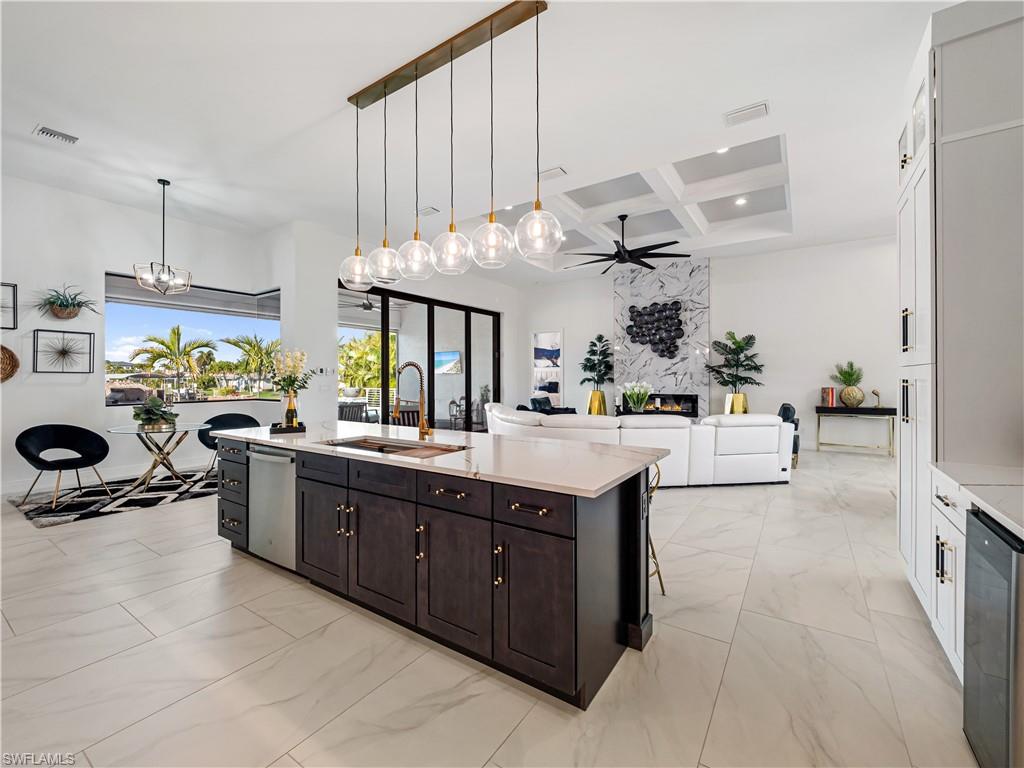 Kitchen with coffered ceiling, open floor plan, light marble finish floors, a center island with sink, and light stone counters