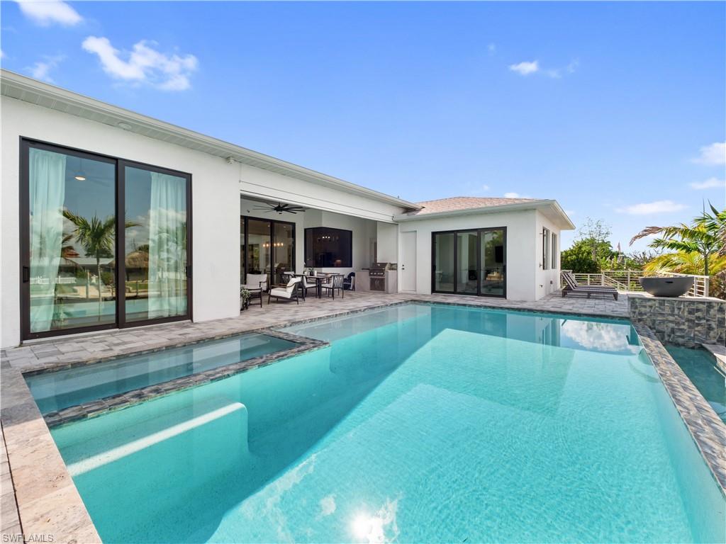 Rear view of house with ceiling fan, a patio area, stucco siding, and a pool with connected hot tub