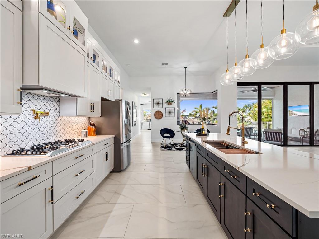 Kitchen with light stone counters, glass insert cabinets, a large island, stainless steel appliances, and pendant lighting
