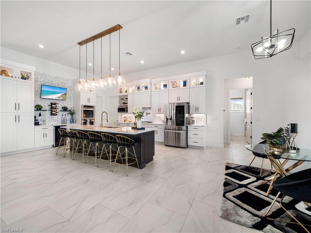 Two tone kitchen featuring glass fronted cabinets, stainless steel appliances, a kitchen breakfast bar, backsplash, and two tone color scheme