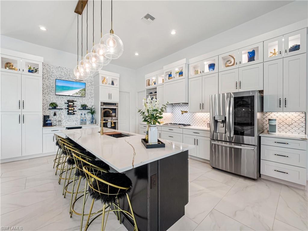 Dual tone kitchen with glass insert cabinets, light marble finish flooring, a breakfast bar area, light stone countertops, and stainless steel appliances